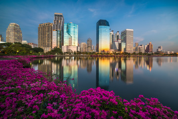 Fototapeta premium Lake with Purple Flowers in City Park under Skyscrapers at Twilight. Benjakiti Park in Bangkok, Thailand