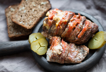 Stuffed pork baked with tomatoes, cheese and spices on a round wooden Board with a pickles and bread on a grey linen napkin 