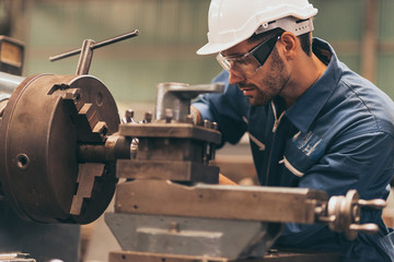 Closeup side view of early 40's male employee at a factory plant operating a production line machine and setting it for work.