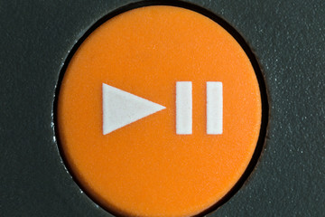 Macro close up photograph of orange play or pause button on vintage portable tape player.  