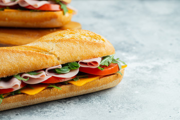 Two Long baguette Sandwiches with arugula, slices of fresh tomatoes, ham and cheese