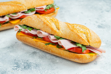 Two Long baguette Sandwiches with arugula, slices of fresh tomatoes, ham and cheese