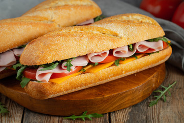 Two Long baguette Sandwiches with arugula, slices of fresh tomatoes, ham and cheese