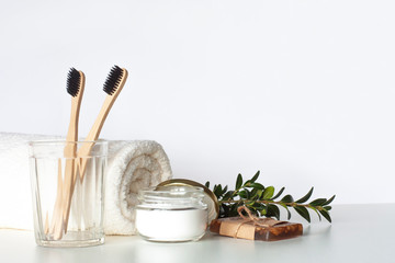 Two bamboo toothbrushes in glass, natural tooth powder, handmade soap and towel on light gray table. Zero waste bathroom, eco friendly morning routine and sustainable lifestyle concept. Copy space.