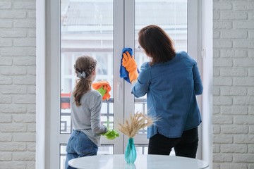 Mother and daughter child in gloves with detergent rag cleaning windows together