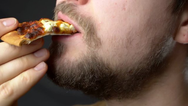 A young man eats cheesy pizza slow motion super close up
