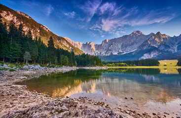 Naklejka na ściany i meble Amazing view on Lago di Fusine Inferiore at sunrise. Splendid morning scene of Julian Alps, Province of Udine, Italy, Europe. Beautiful forests are reflected in the quiet lake. Dolomites mountains.