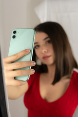 A young brunette girl with short hair and red shirt taking a selfie next to the mirror with her cell phone