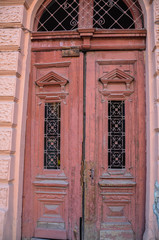 Broken old double red doors with broken windows and faded peeling paint in a pink stone frame