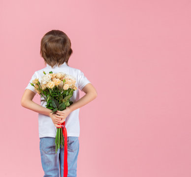Boy Holds A Bouquet Of Flowers Behind His Back On A Pink Background. Concept Of Holidays, Birthday, Valentine's Day And Mothers Day.