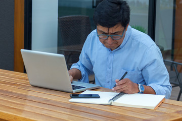 man with glasses working with his computer, his cell phone and a notebook