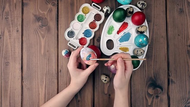 Hand painted Easter eggs, paints and brushes on wooden background. Preparation for the holiday. Girls hands draw a pattern