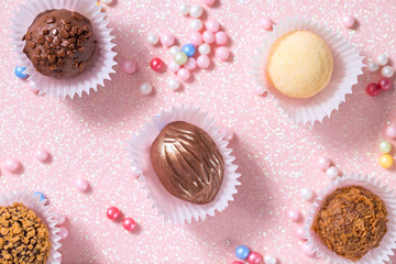 Chocolate, nut and coconut candies on a pink background, decorated with sugar sprinkles of candy, top view