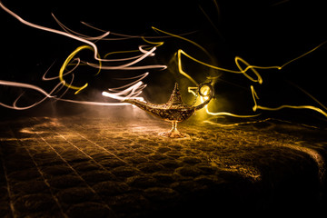 Lamp of wishes concept. Antique Aladdin arabian nights genie style oil lamp with soft light white smoke, Dark background.