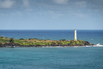 Fototapeta premium Nawiliwili, Kauai, Hawaii, USA. - January 17, 2020: Yellow Ninini lighthouse on black ocean-shore rocks of its green lands end. Blue ocean and sky..