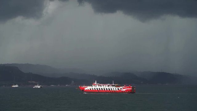 A passenger ferry sails toward island in front of a dark rain storm, Slow motion, East Java Indonesia