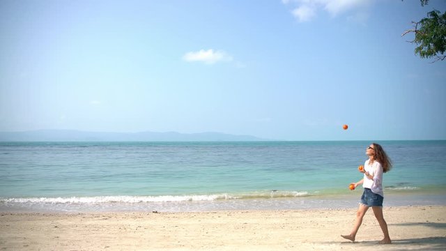 Young cheerful woman juggles tangerines on the beach on a sunny day. Having fun on the vacation.