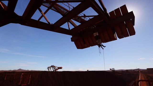 Silhouette HD footage of male industry rope access technician inspector abseiler abseiling safety descending with twin low stretch rope working at height inspecting concrete spalling on counterweight 