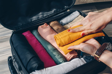 Top view of tourist woman open suitcase for pack and arranging colorful cloths for travelling....