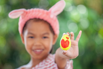 Happy asian child girl drawing heart picture on egg and holding painted easter egg with fun in easter festive.