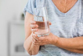 Senior woman suffering from Parkinson syndrome with glass of water in clinic, closeup