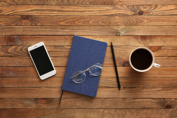 Notebook with mobile phone, cup of coffee and eyeglasses on wooden table
