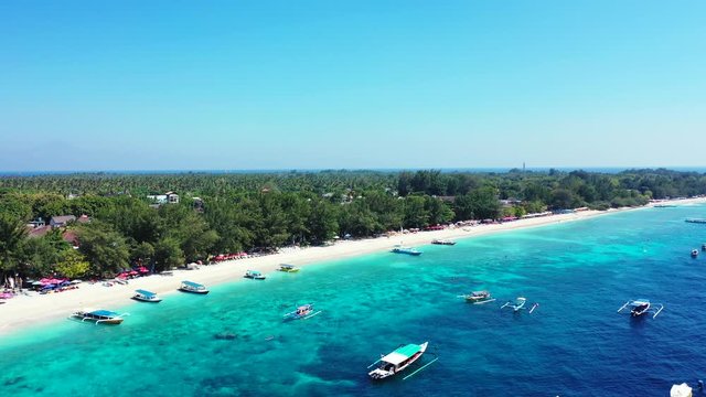 Vivid colors of Balinese island coastline with tourist boats floating over blue azure sea water near white sandy beach