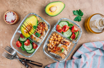 Healthy meal prep containers with chickpeas, chicken, tomatoes, cucumbers and avocados. Healthy lunch in glass containers on beige rustic background. Zero waste concept. Selective focus.