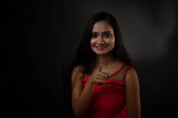 Obraz na płótnie Canvas Fashion portrait of an young and attractive Indian Bengali brunette girl in red western dress in front of a black studio background. Indian fashion portrait and lifestyle.