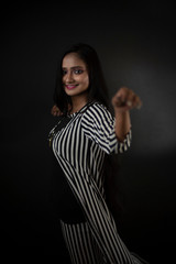 Fashion portrait of an young and attractive Indian Bengali brunette girl with striped western semi formal/casual dress in front of a black studio background. Indian fashion portrait and lifestyle.