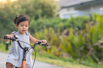 Fototapeta na wymiar Cute Little Girl Riding Her Orange Bike in the Park 