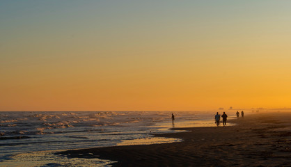 Tranquil beach scene at Port Aransas, Texas at sunset with waves, clear sky and silhouette of a few people.