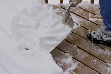 Fototapeta na wymiar Close up view of an unseen person shoveling deep snow of a wooden deck surface