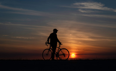Cyclist standing next to bike, alone at sunset in natural setting