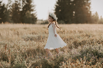 happy joyful young girl in a white dress and with a flower wreath on her head in the field in the...