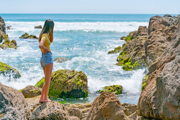 Girl in yellow top on coastal rocky seaside.