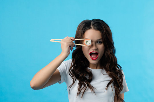 Portrait of a brunette girl who has hadi sushi in her hands. The girl opened her mouth wide in surprise. She brought sushi to her eye
