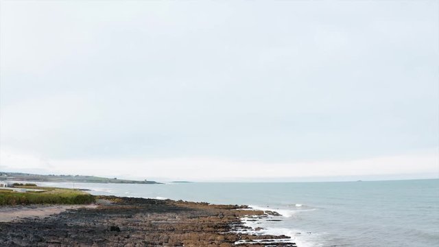 The coastline of Skerries in Ireland. The camera starts moving from top to down while showing the small waves at the coast.