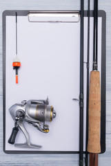 close-up of the wooden handle of a fishing rod, reel with fishing line and float, on a sheet of paper, with a place for writing