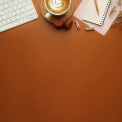 Flat lay, top view office table desk. Workspace with blank clip board, notebook, office supplies, pencil, green leaf, and coffee cup on brown background