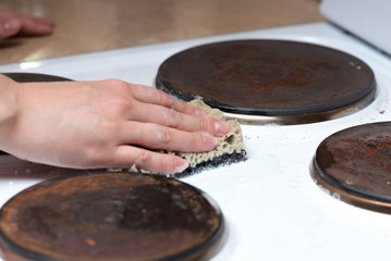 Woman is washing the surface of the electric stove with a cleaner close up.