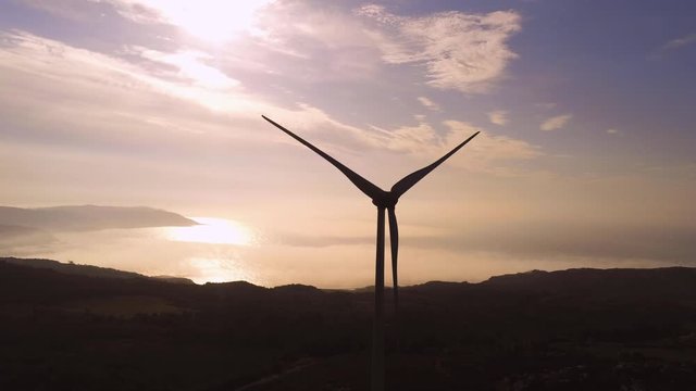 Wind turbine rotating during sunset. Aerial zoom out