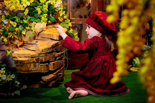 Small girl with little chicken in village interior in studio full of flower. Easter, holiday and child concept