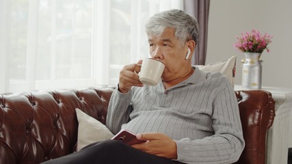 Senior man use wireless earphone listening music and drink coffee