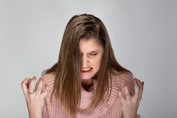 Close up portrait of a young Caucasian woman wearing a pink sweater on a grey background. She looks...