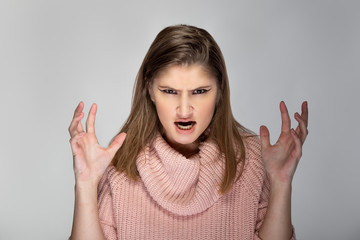 Close up portrait of a young Caucasian woman wearing a pink sweater on a grey background. She looks...