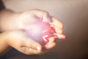 光を放つ沢山の赤いハートのモチーフを持つ子供の手