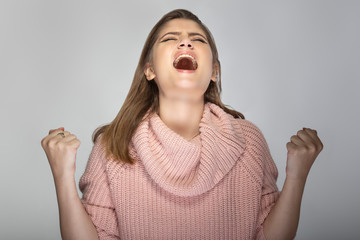 Close up portrait of a young Caucasian woman wearing a pink sweater on a grey background. She looks...