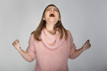 Close up portrait of a young Caucasian woman wearing a pink sweater on a grey background. She looks...