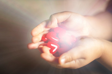 光を放つ沢山の赤いハートのモチーフを持つ子供の手